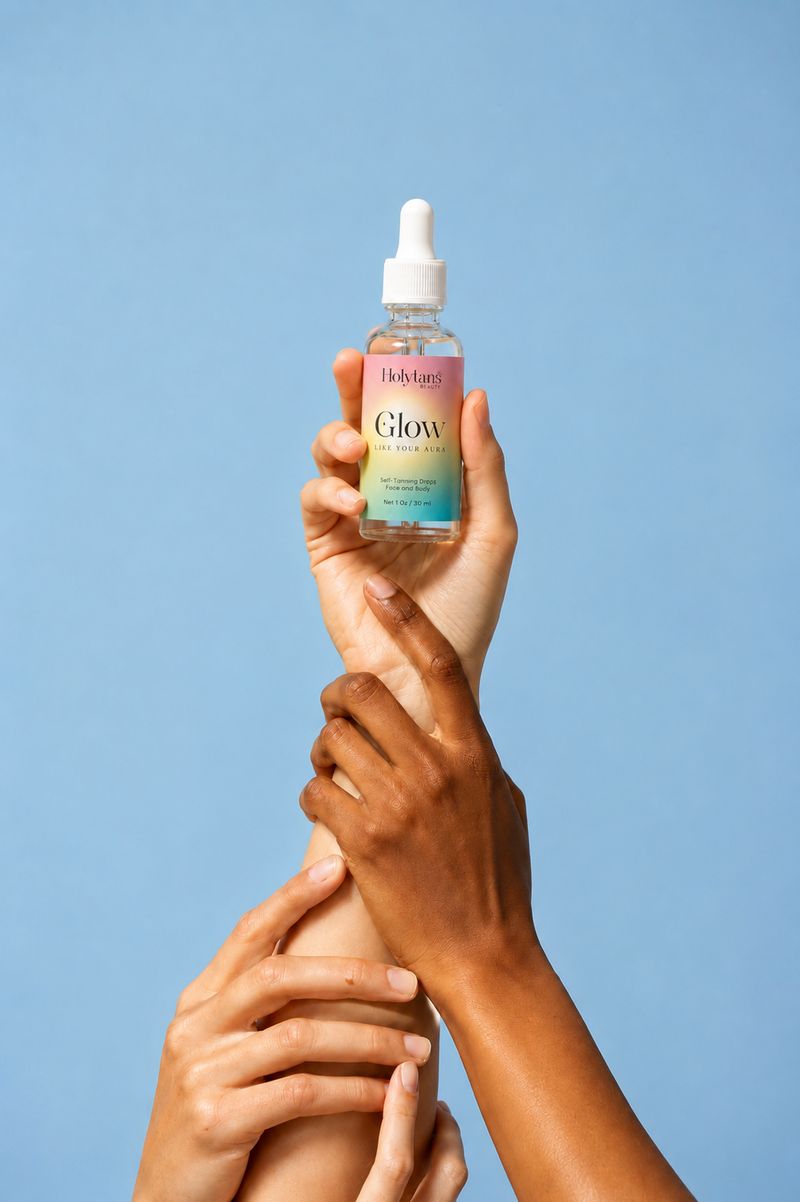 GLOW self tanning drops held up by hands of different skin tones